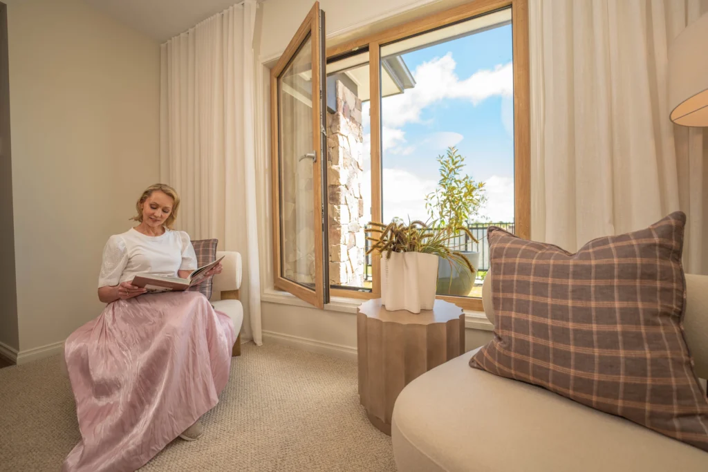 Lady in a pink skirt reading a book next to a open window